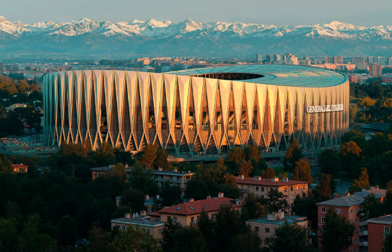 Modernes Stadion mit auffälliger Fassade vor schneebedeckten Bergen und Stadt im Hintergrund.