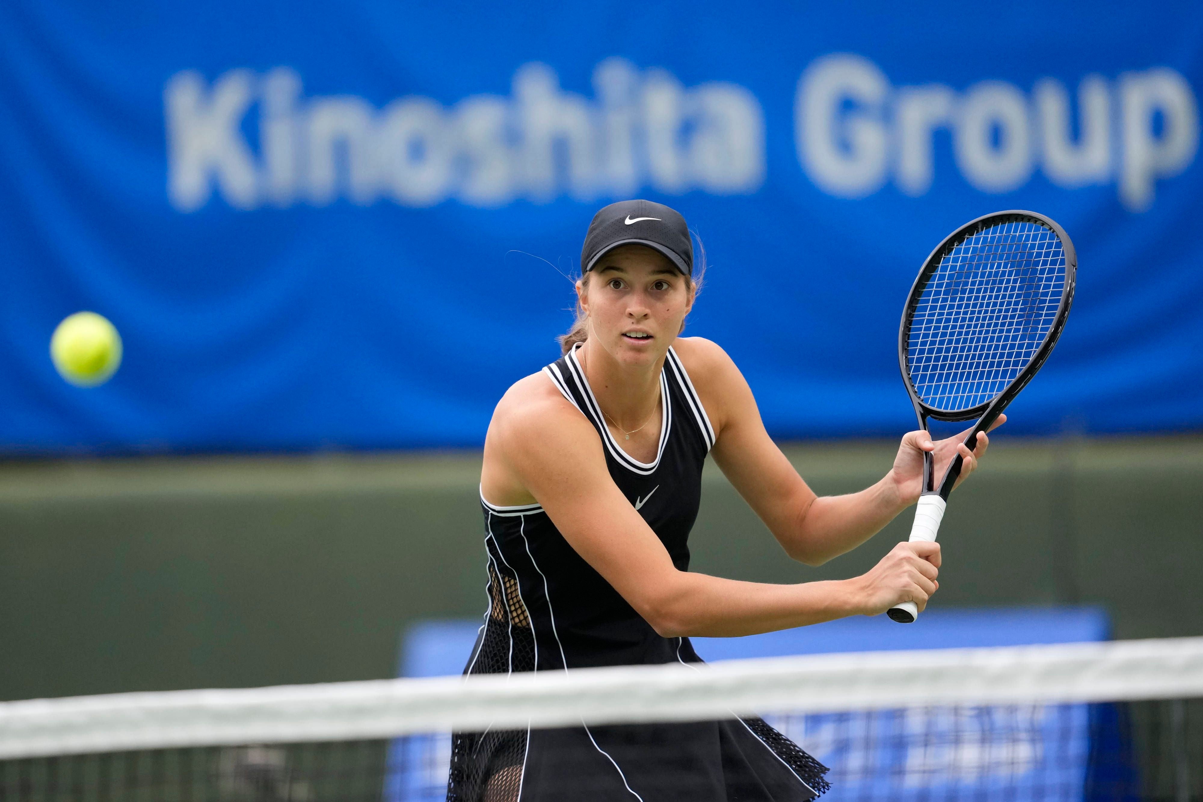 Eine Tennisspielerin schlägt einen Ball während eines Doppeltspiels in einer Halle.