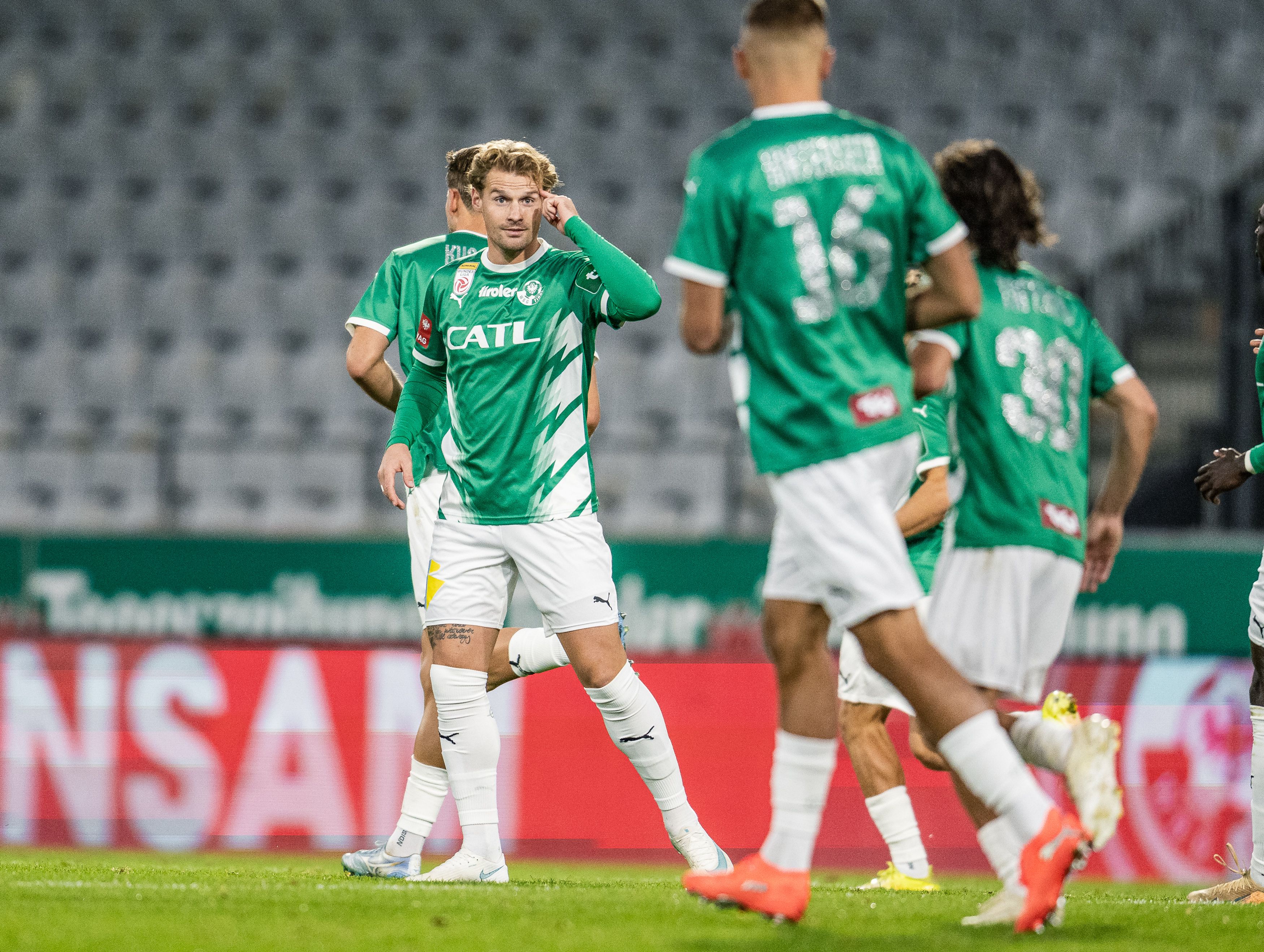 Thomas Goiginger im grünen WSG-Tirol-Trikot tippt sich mit dem Zeigefinger an den Kopf, während seine Mitspieler im Hintergrund stehen.