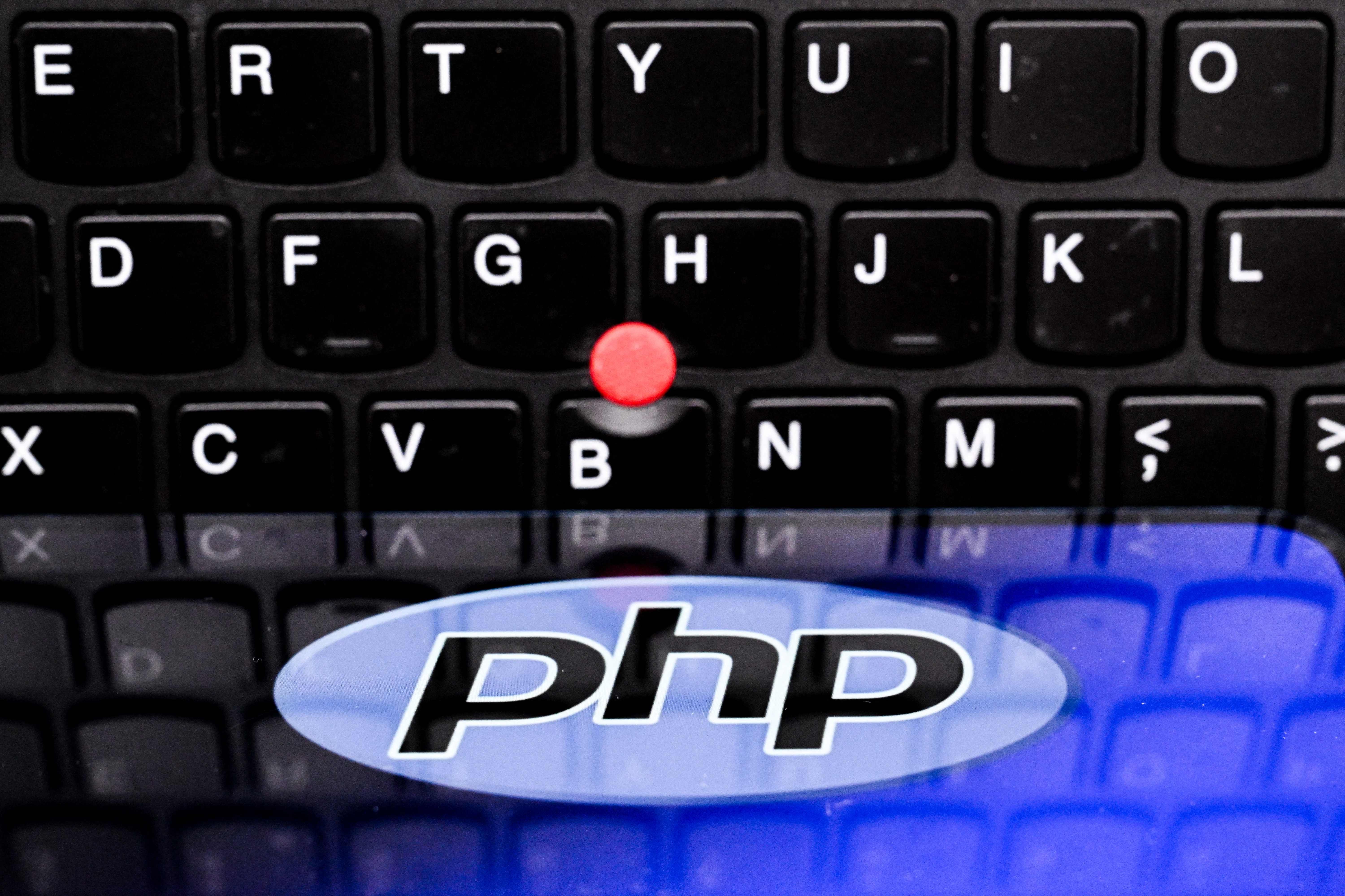 Das PHP-Logo ist auf einem Smartphone vor einer schwarzen Laptop-Tastatur zu sehen.