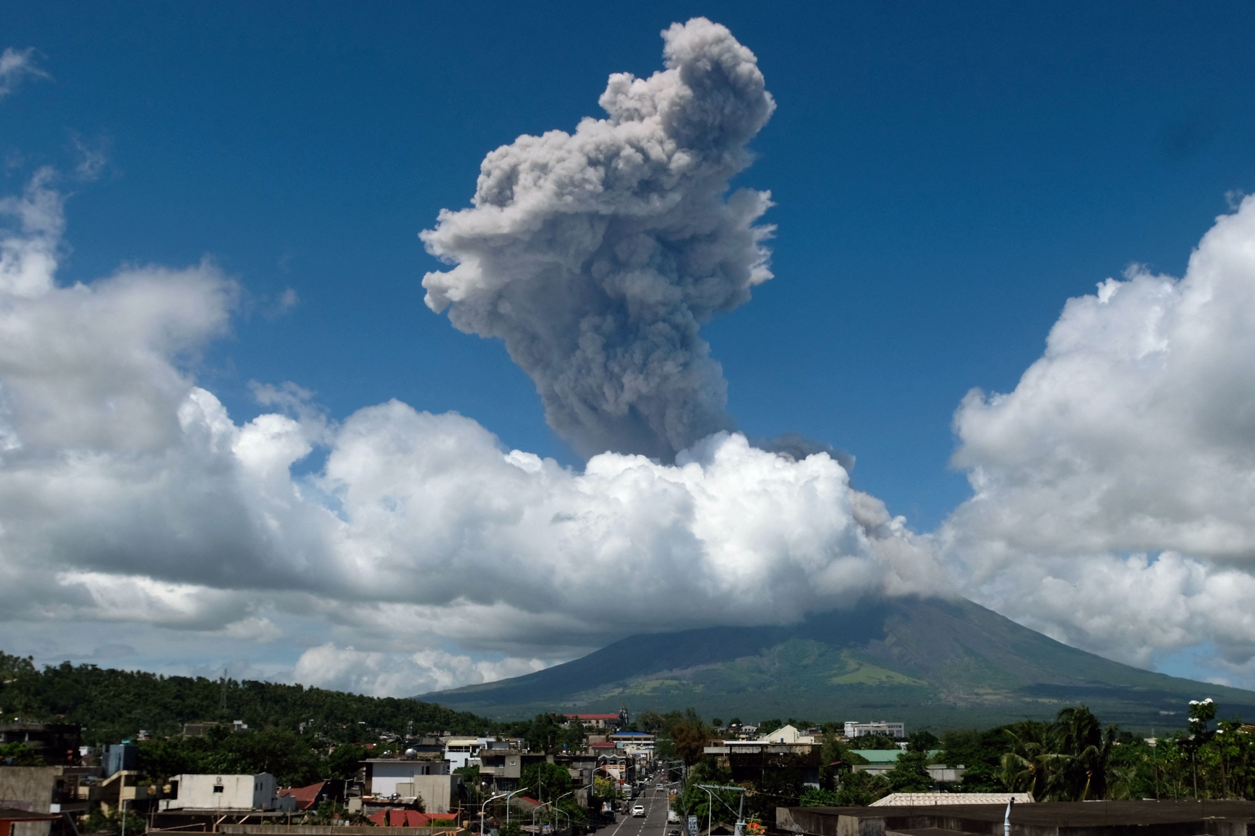 Eine große Aschewolke steigt bei einem Vulkanausbruch aus dem Mayon-Vulkan hinter einer Stadt auf.