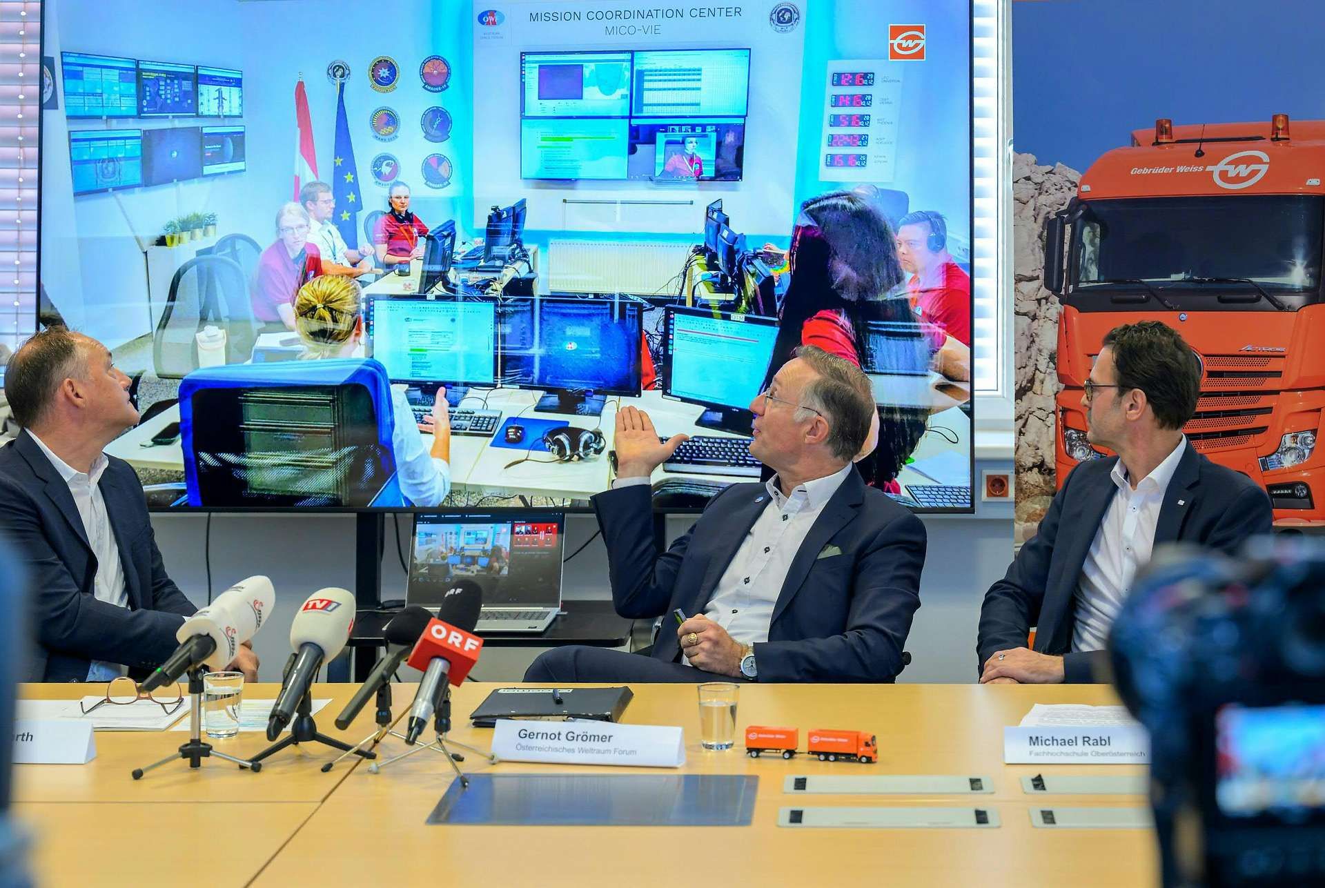 Drei Männer sitzen vor Mikrofonen und Monitoren bei einer Mars-Mission-Trainingsbesprechung.