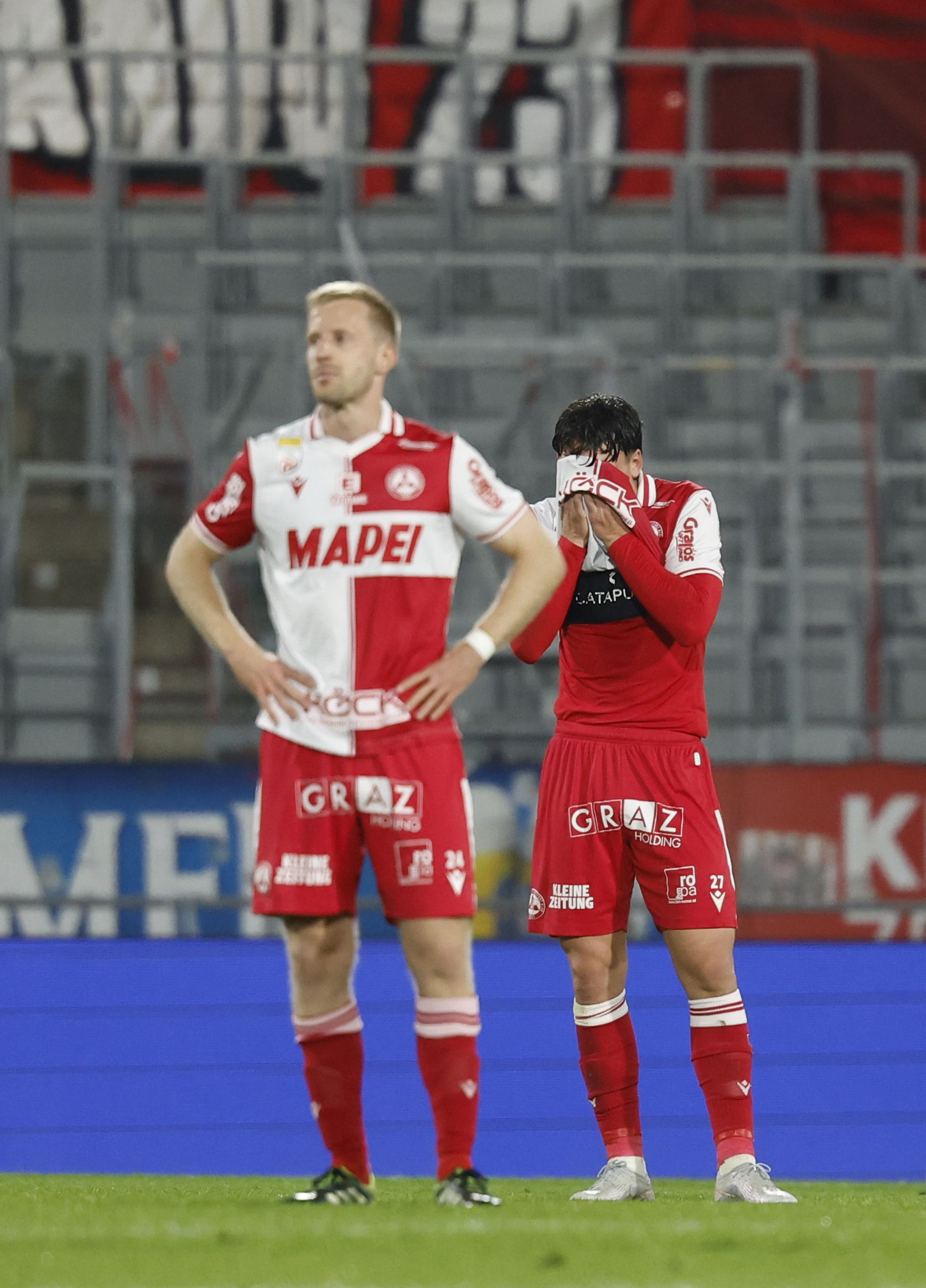 Ein enttäuschter GAK-Spieler schlägt sich das Trikot über das Gesicht, während ein Mitspieler mit gesenktem Kopf daneben steht.