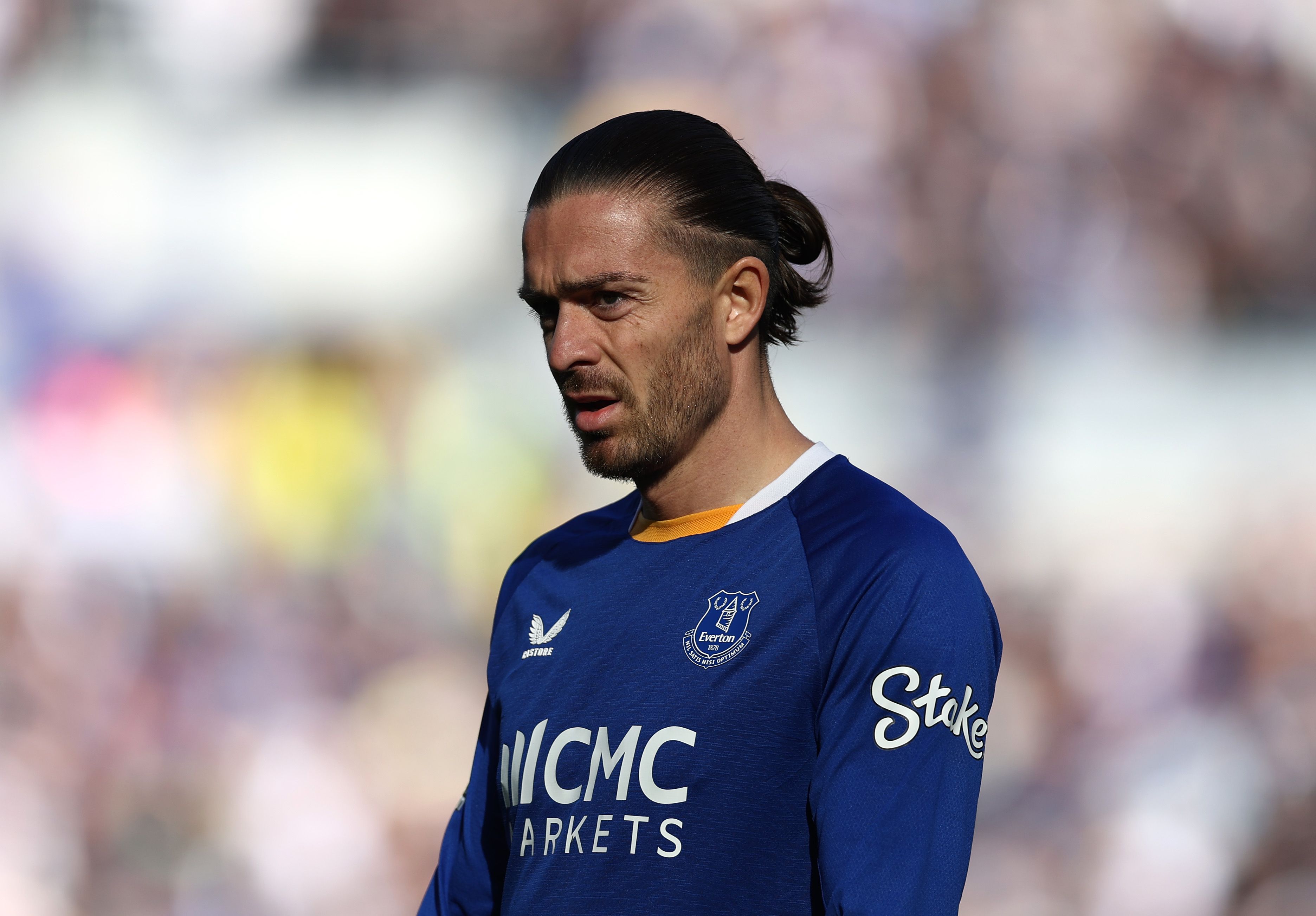 Jack Grealish blickt im blau-weißen Trikot des FC Everton mit zusammengebundenem Haar nachdenklich zur Seite.