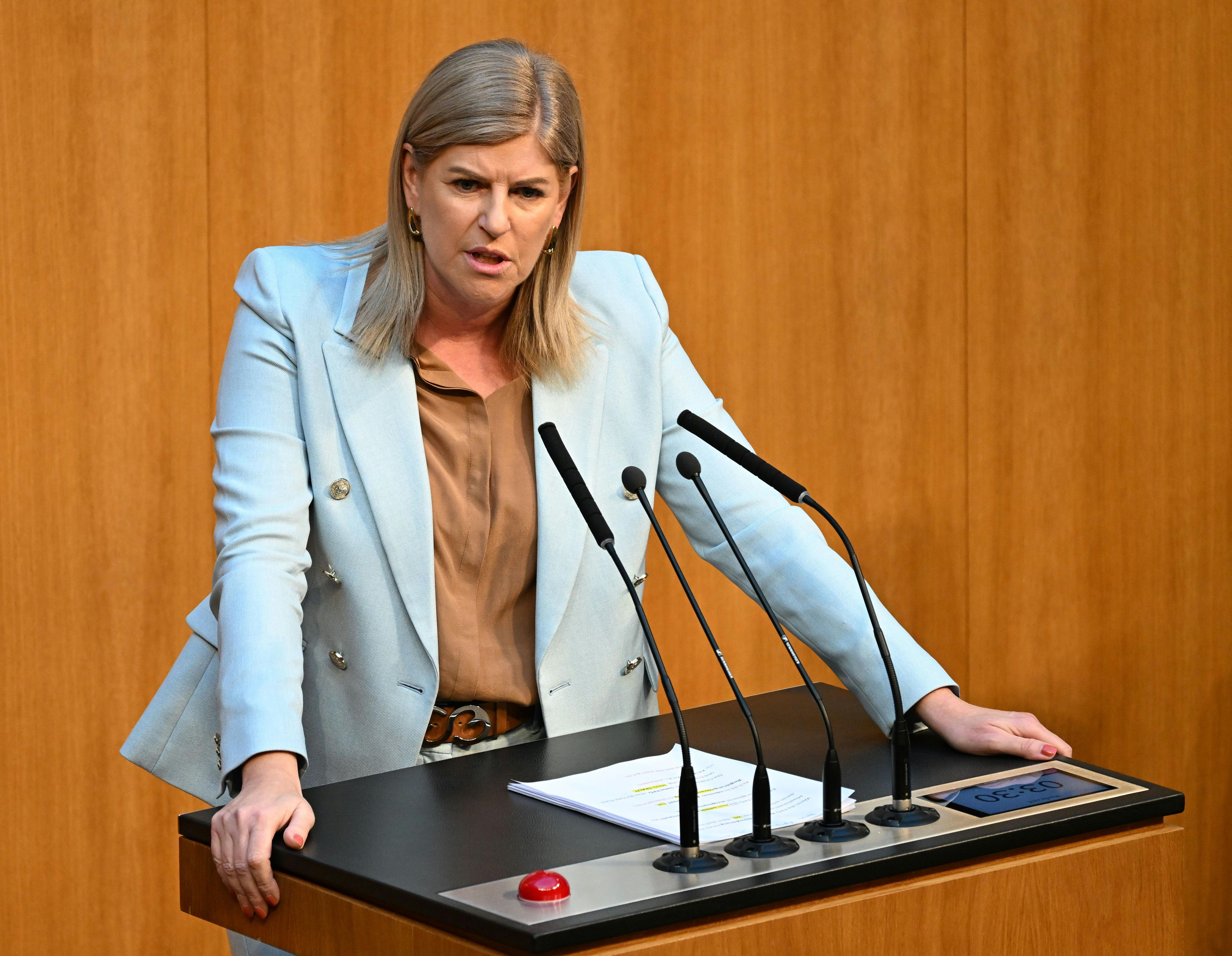 Eine Frau spricht ernsthaft an einem Rednerpult im Parlament vor Mikrofonen.
