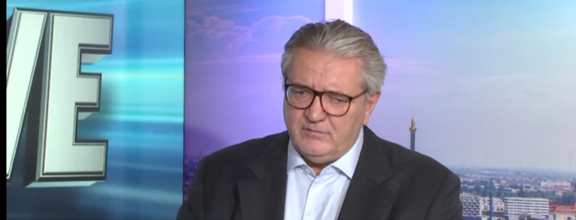 Ein Mann mit Brille und grauen Haaren spricht in einem Fernsehstudio.