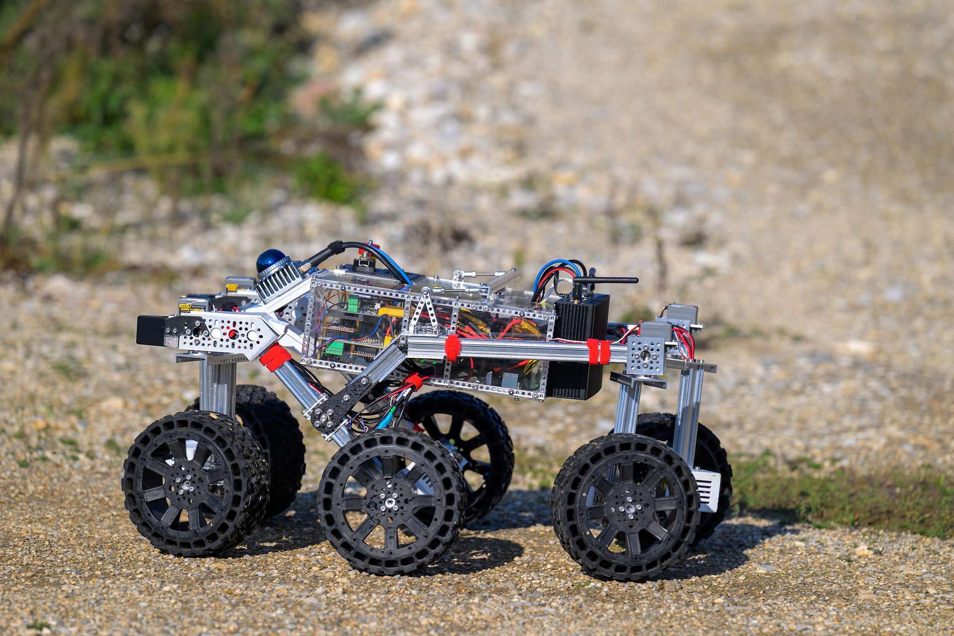 Ein sechsrädriger Mars-Rover-Roboter steht auf sandigem, unebenem Boden im Freien.