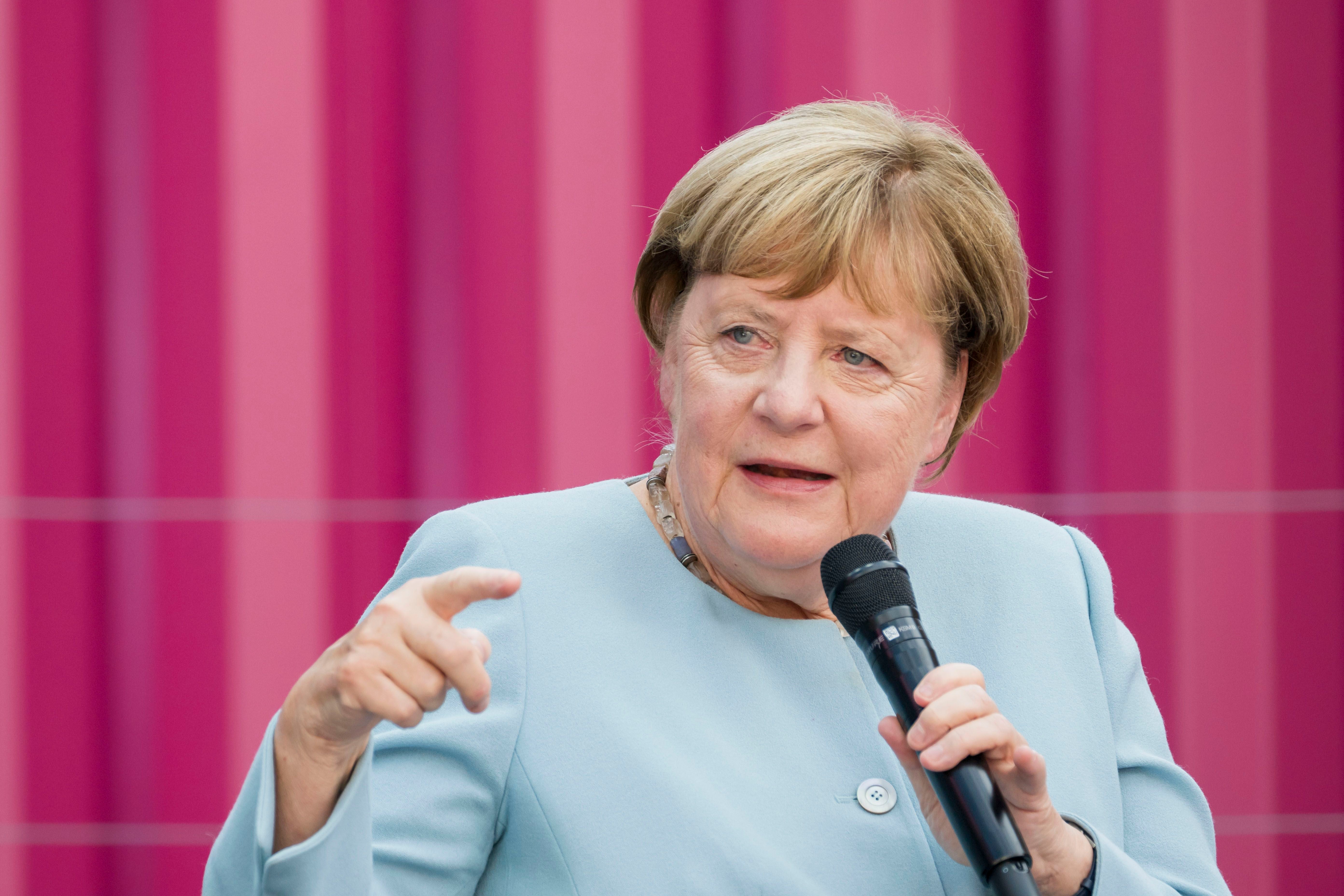 Frau in blauem Blazer spricht mit Mikrofon vor einem pinken gestreiften Hintergrund.