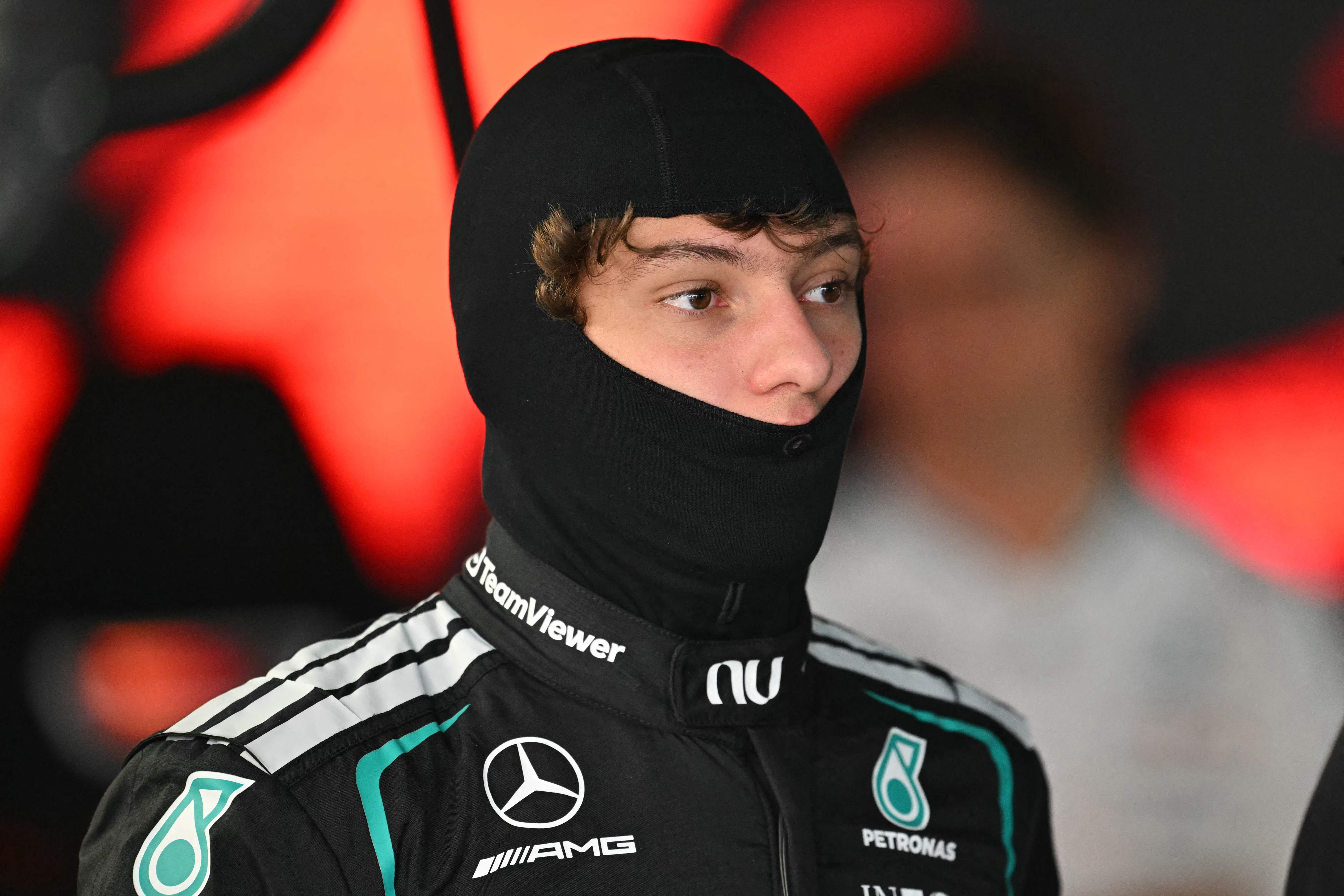Kimi Antonelli blickt im Rennanzug von Mercedes mit schwarzer Sturmhaube aufmerksam in der Boxengasse zur Seite.