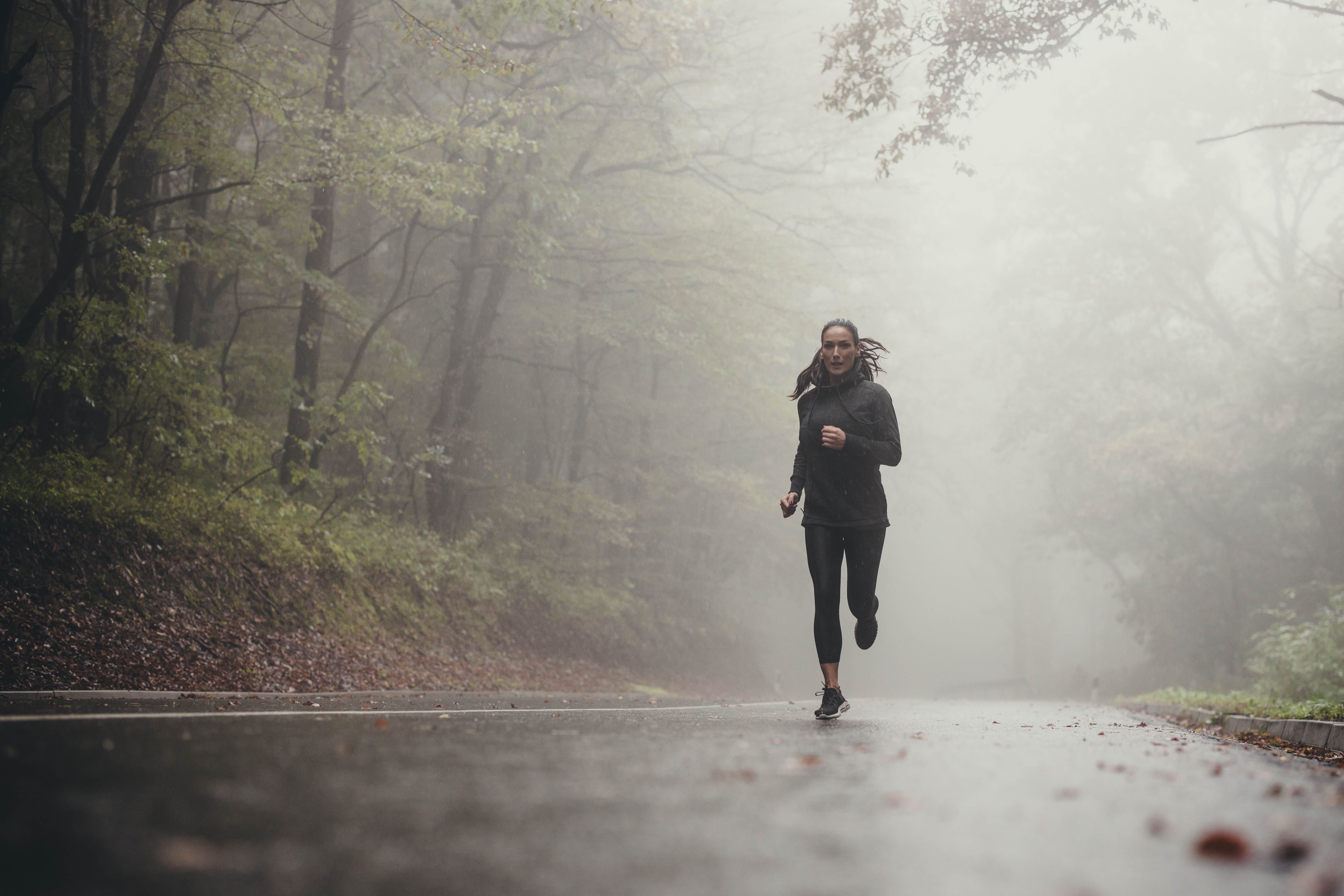Frau joggt auf nasser Straße im nebligen Wald bei Regen.