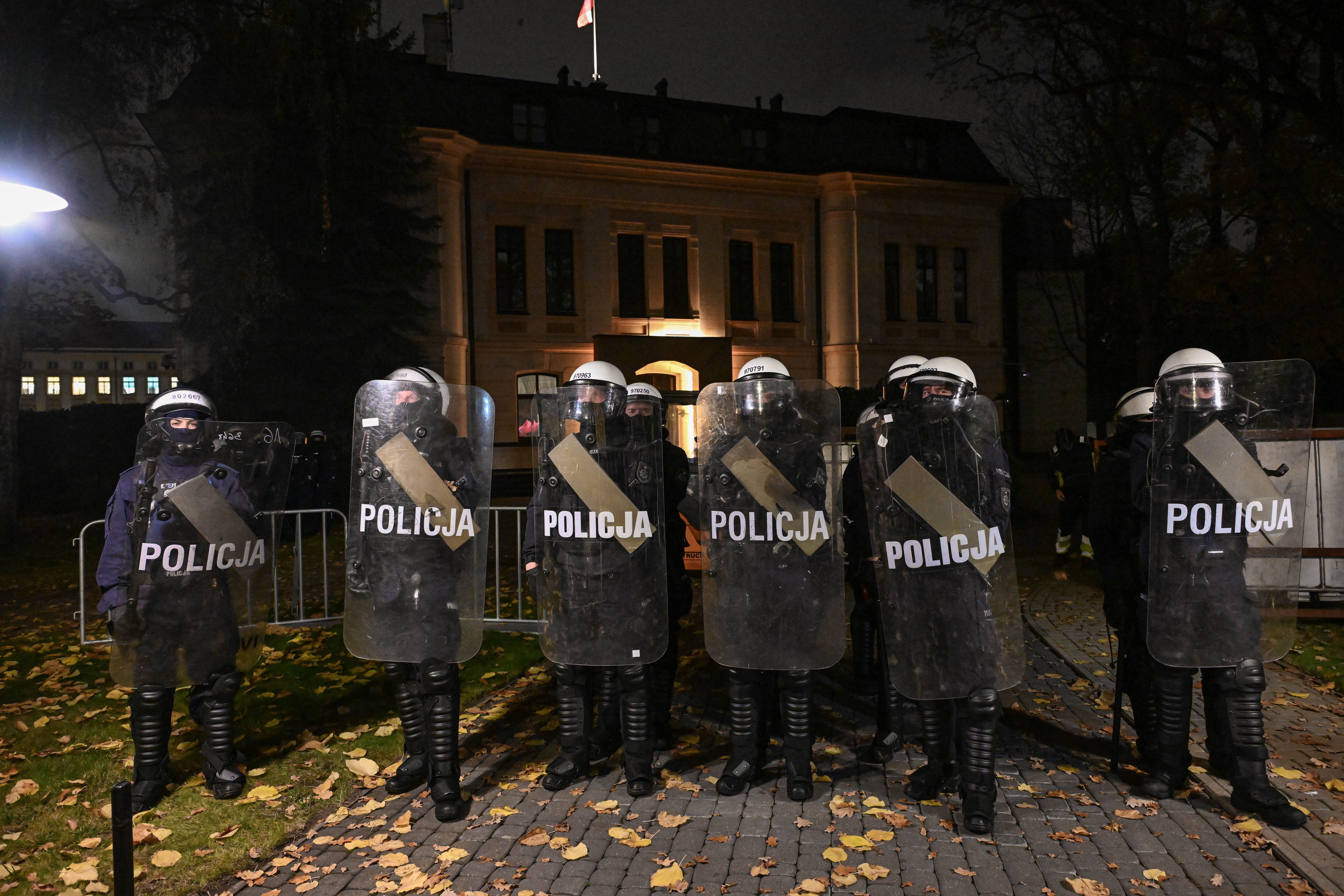 Polizisten in Kampfmontur mit Schilden stehen nachts vor einem beleuchteten Gebäude in Warschau.