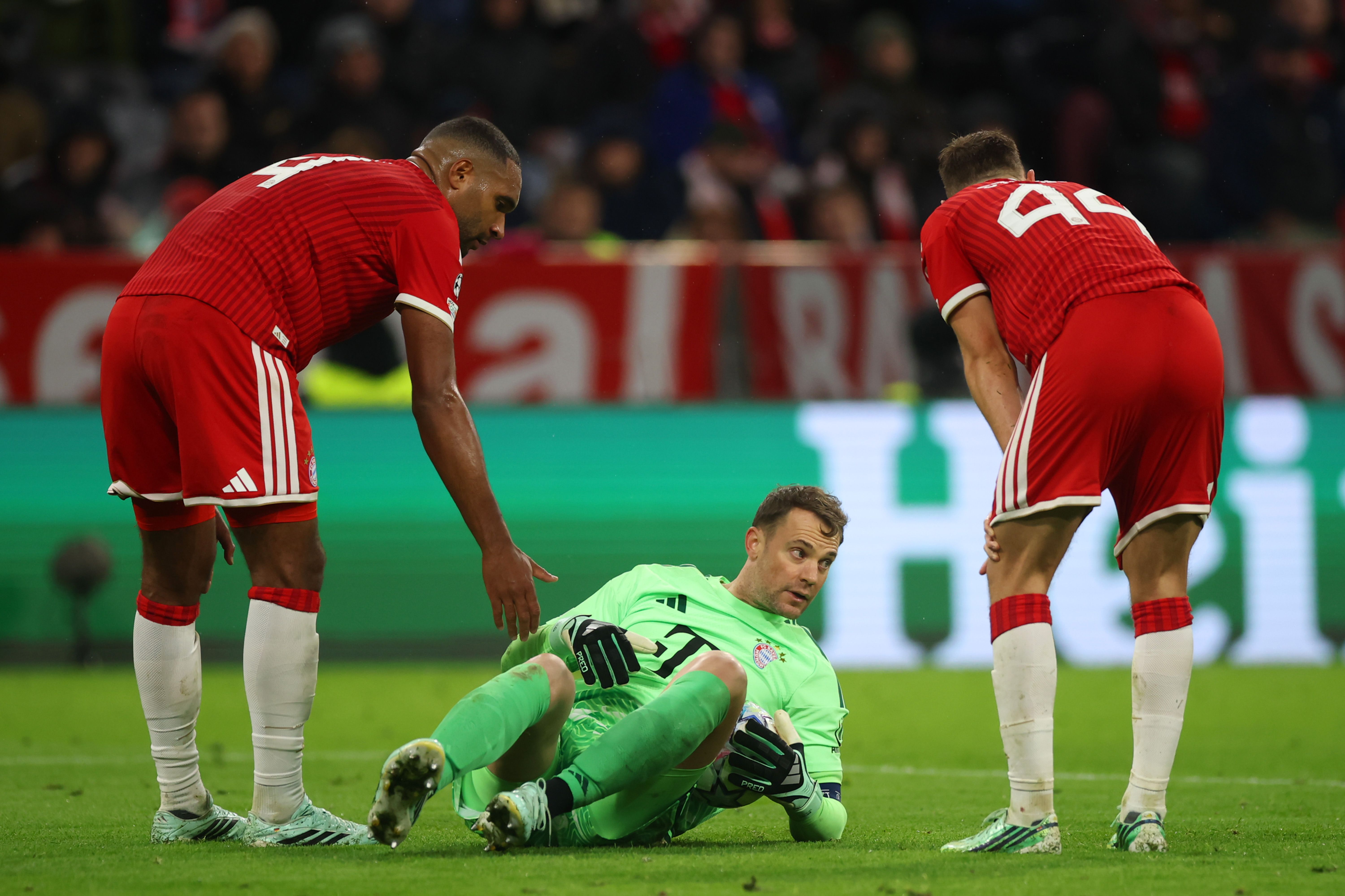 Manuel Neuer sitzt im hellgrünen Torwarttrikot am Rasen und schaut besorgt auf, während Teamkollegen neben ihm stehen.