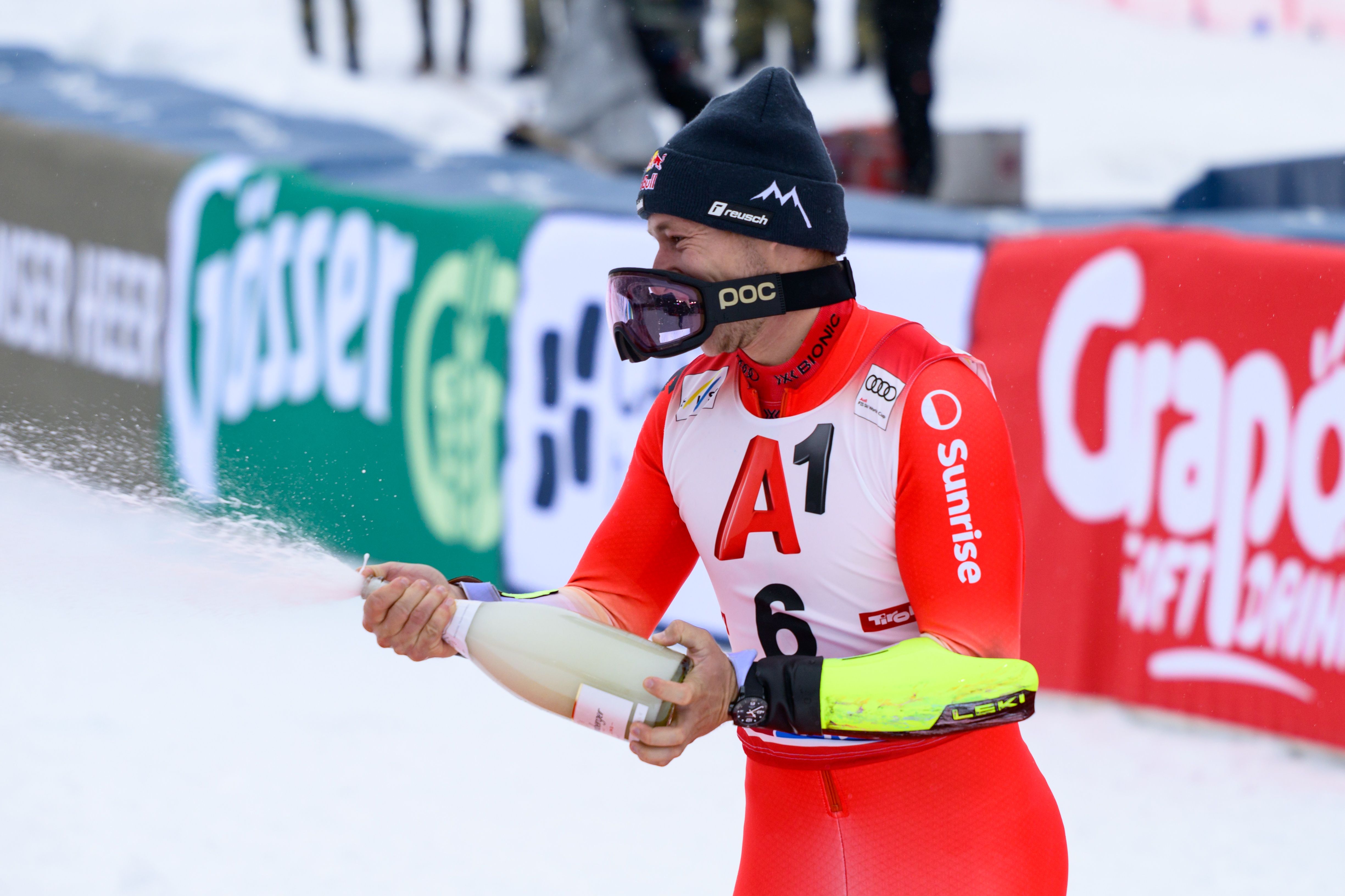 Ein Skifahrer feiert auf dem Podium mit einer spritzenden Champagnerflasche im Schnee.