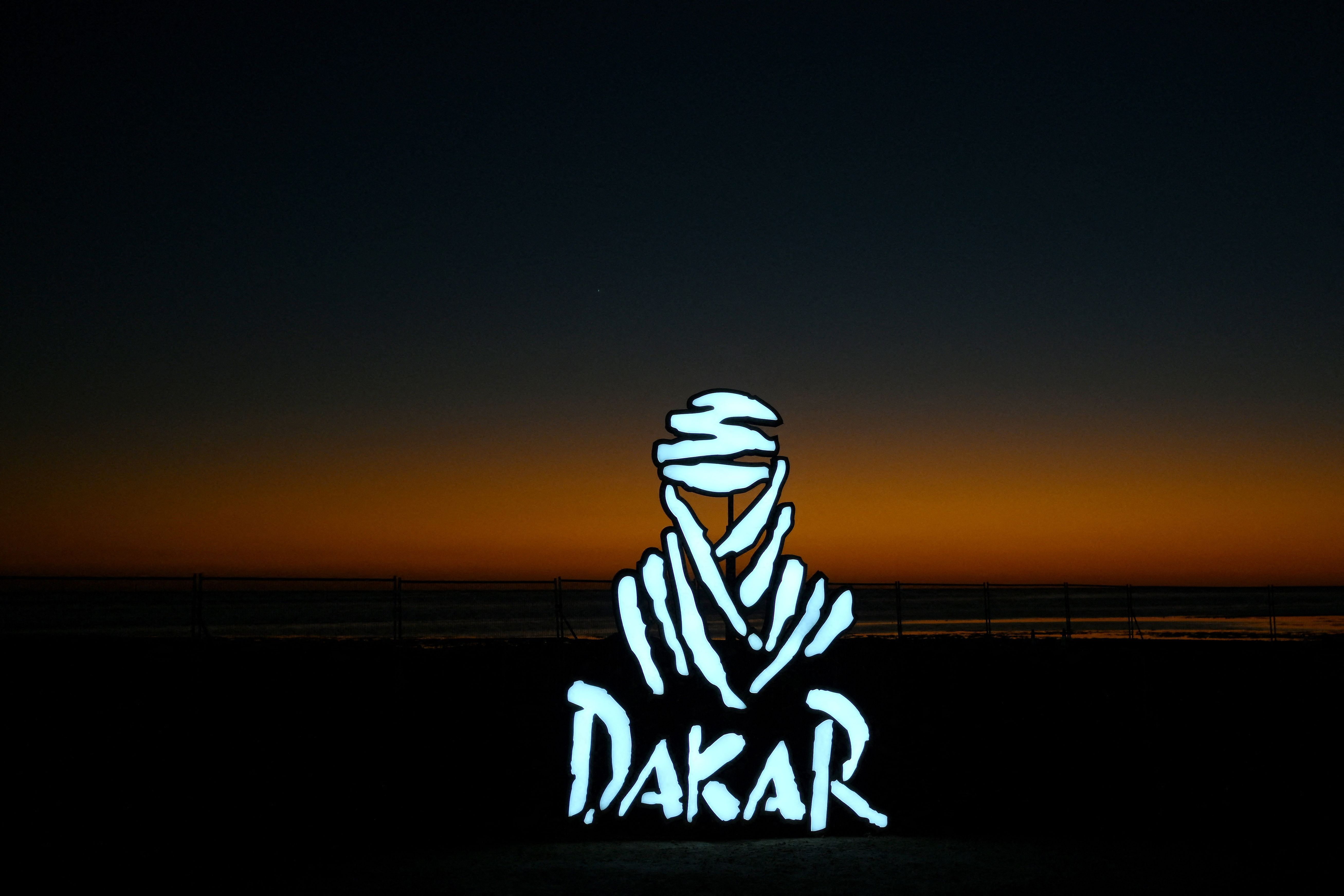 Leuchtendes Dakar Rallye-Logo vor einem Sonnenuntergang am Roten Meer.