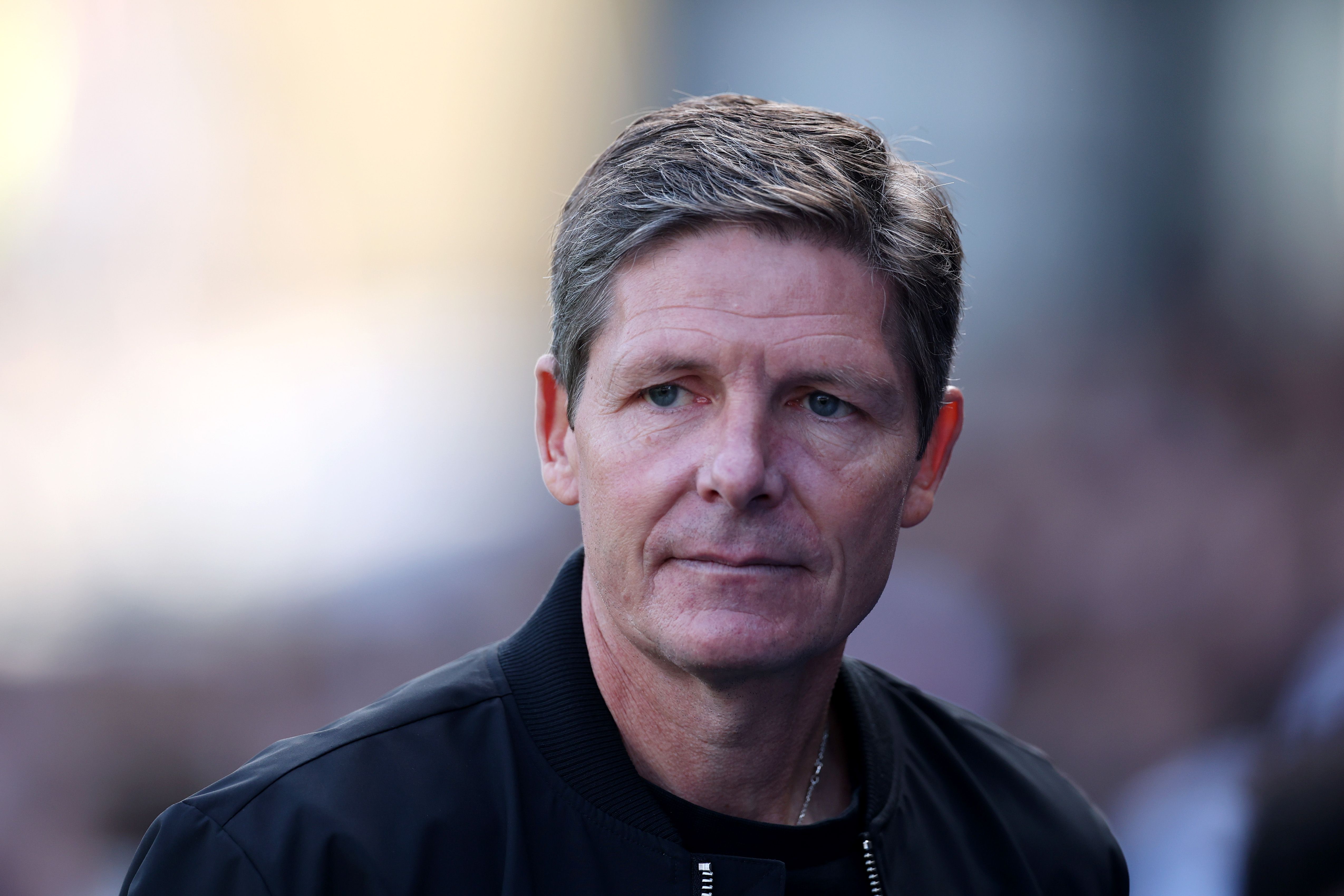 Ein Mann mit kurzen braunen Haaren blickt ernst, im Hintergrund ist alles unscharf.