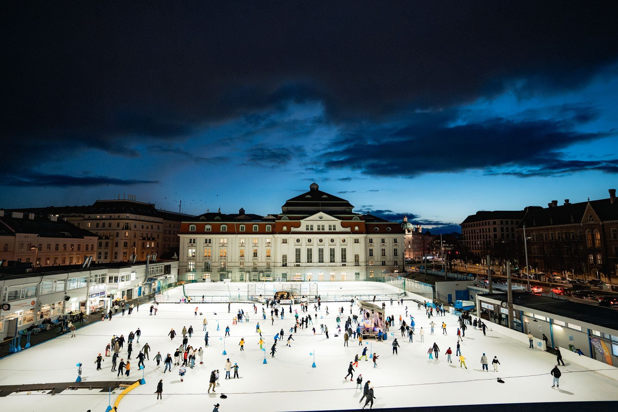 Viele Menschen laufen abends auf einer großen beleuchteten Eislaufbahn in der Stadt.