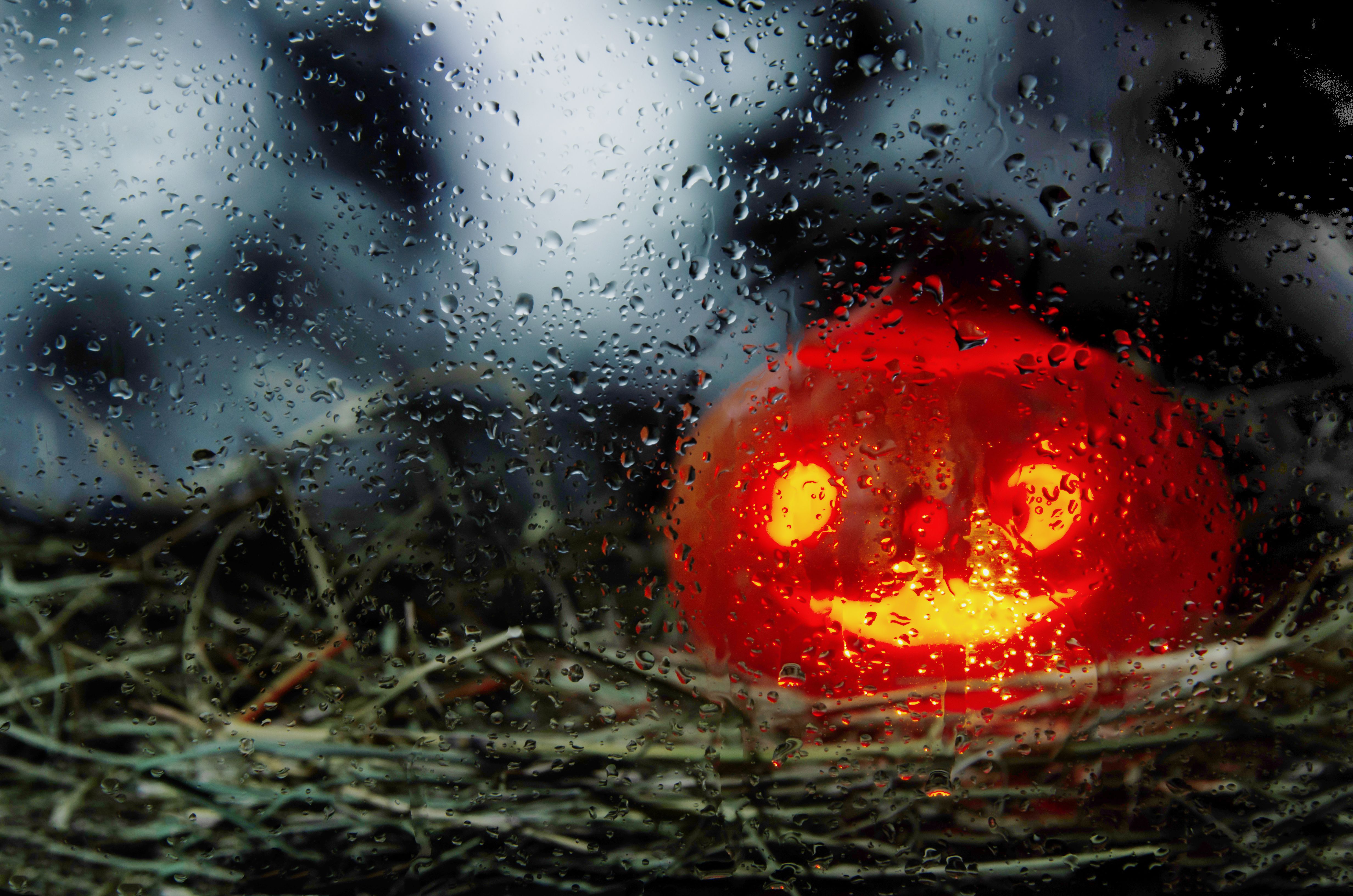 Leuchtender Halloween-Kürbis hinter verregneter Glasscheibe auf Stroh.