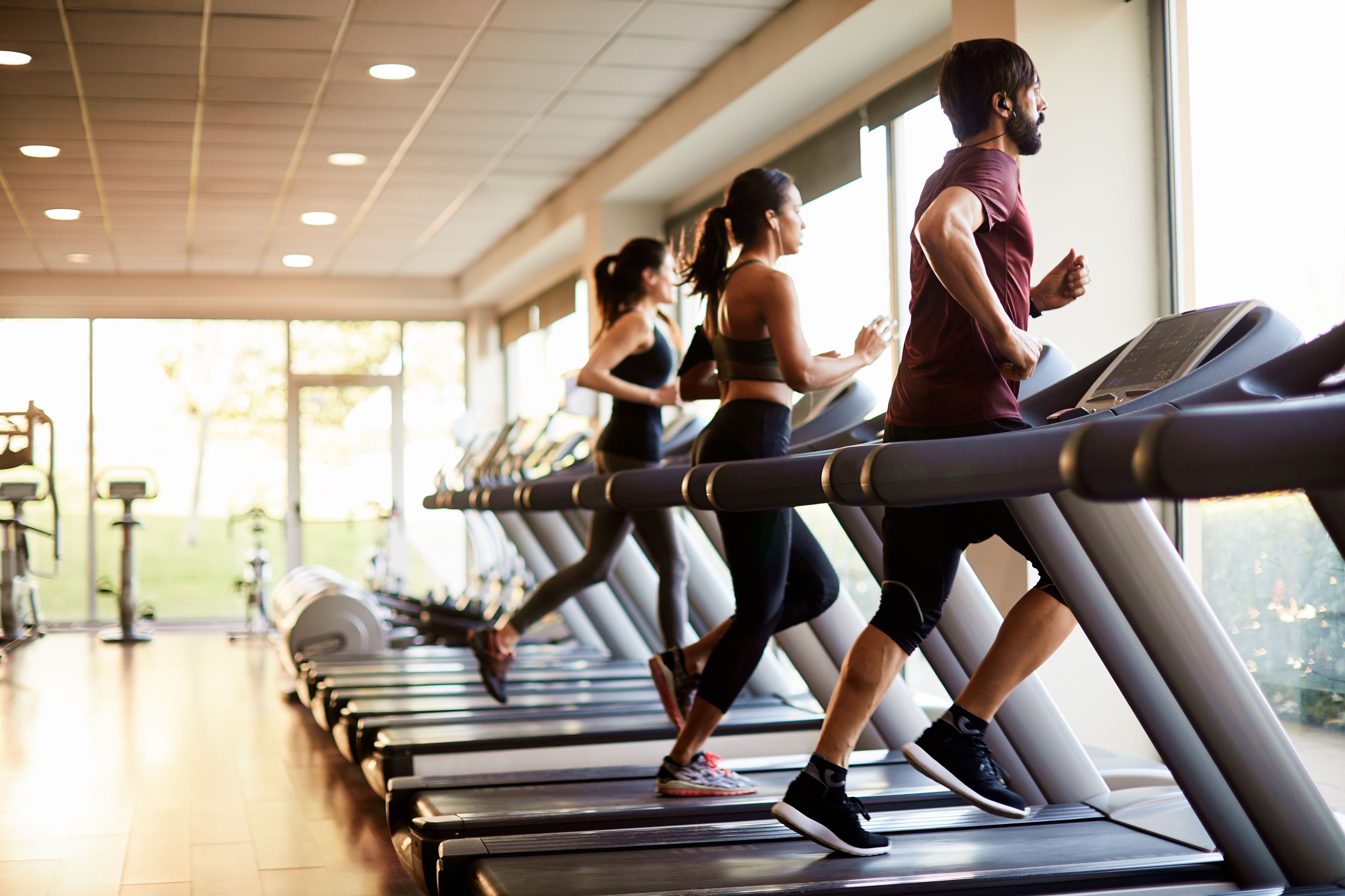 Drei Personen laufen nebeneinander auf Laufbändern in einem hellen Fitnessstudio.
