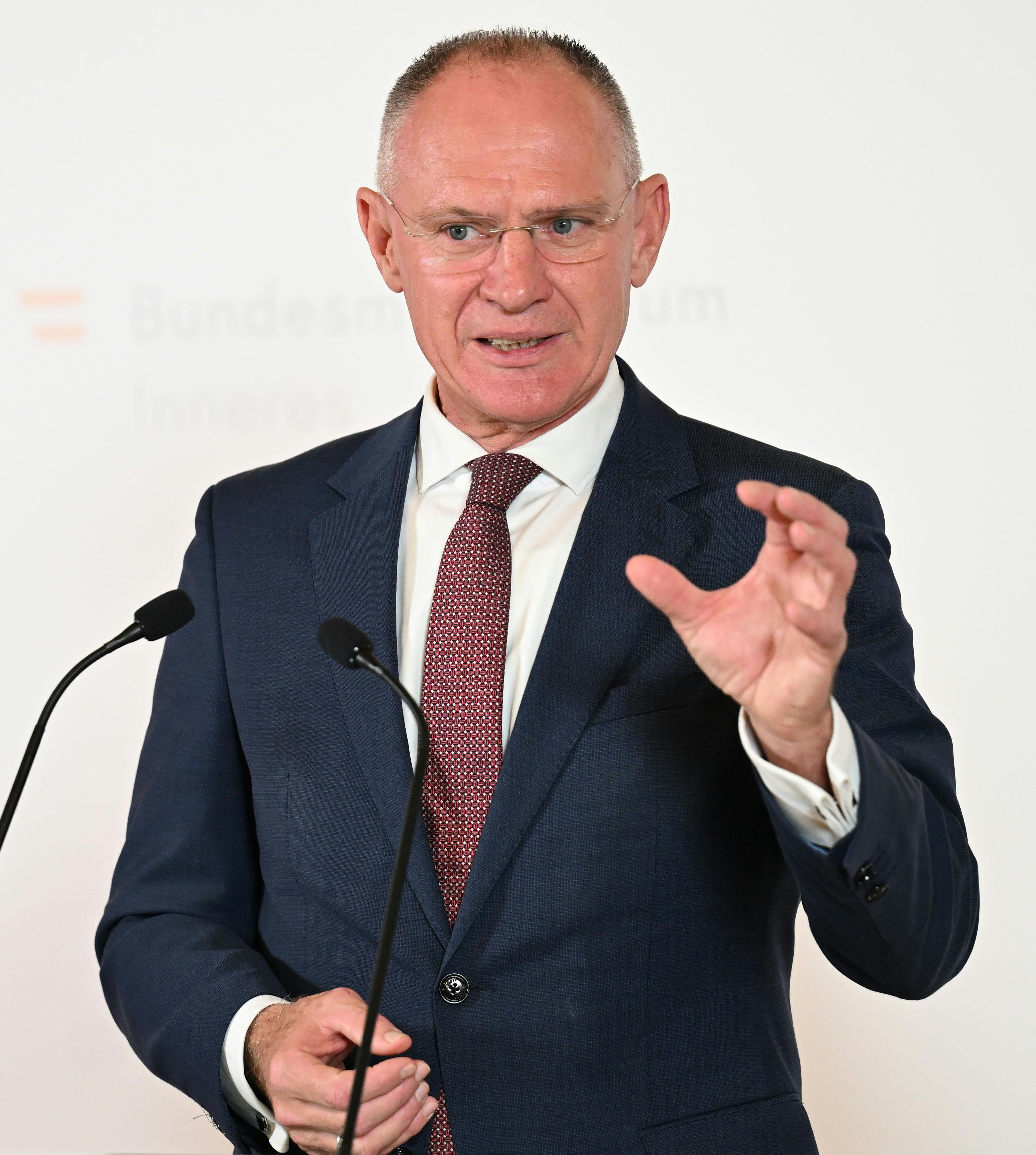 Ein Mann im Anzug spricht bei einer Pressekonferenz am Rednerpult mit Gestik.