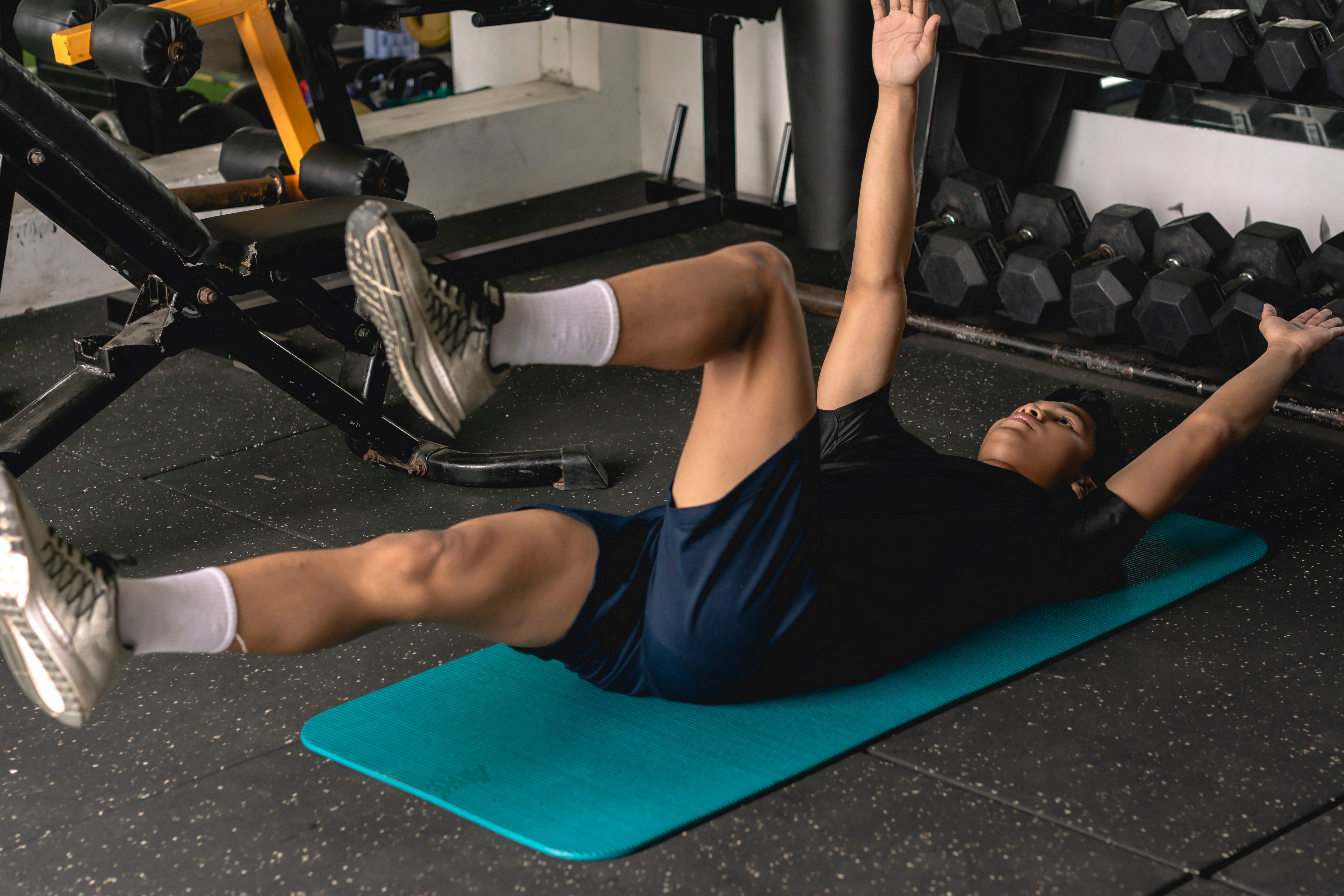 Ein junger Mann macht Dead-Bug-Übungen auf einer Matte im Fitnessstudio.