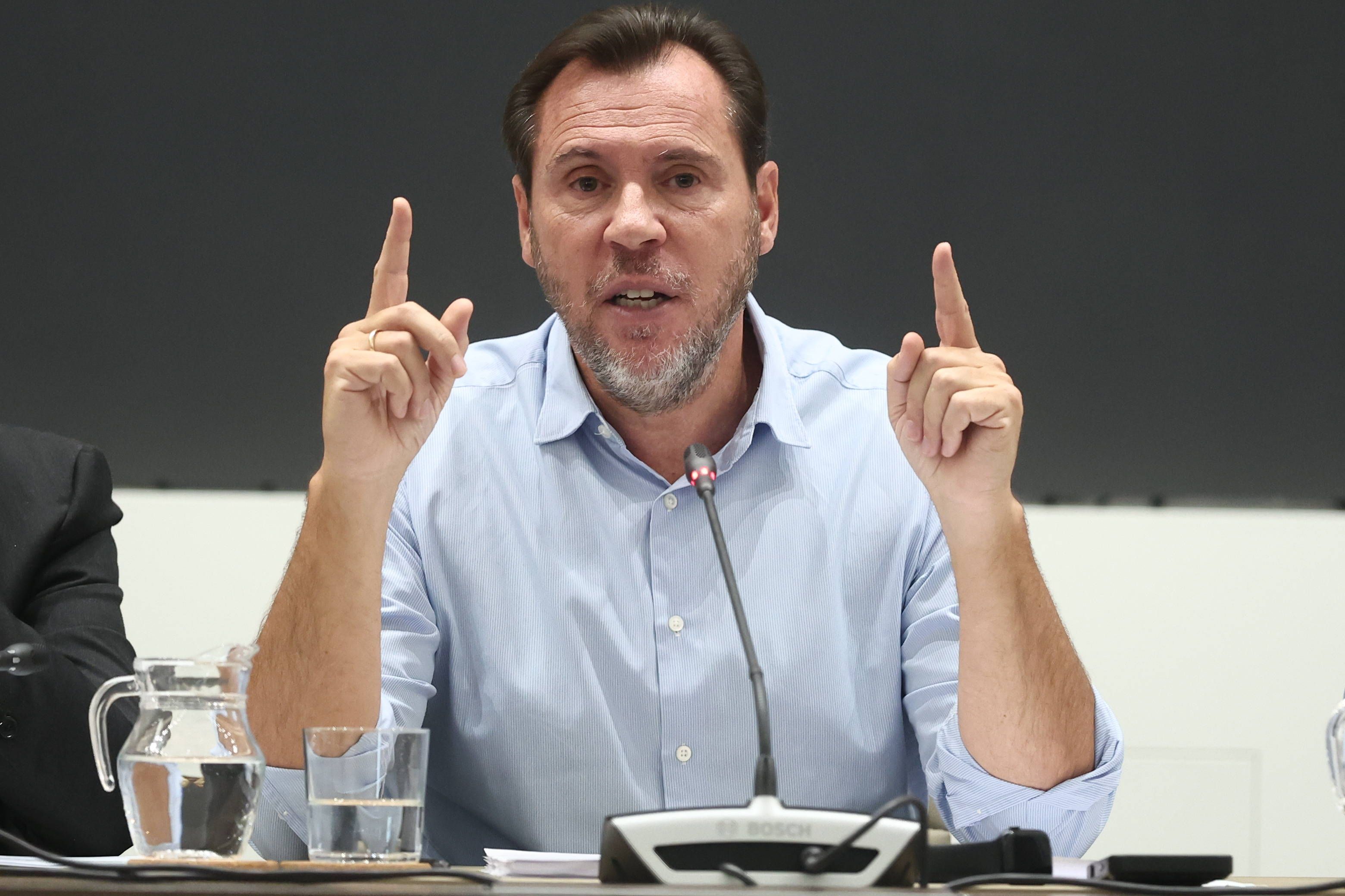 Ein Mann spricht auf einer Pressekonferenz und gestikuliert mit beiden erhobenen Zeigefingern.