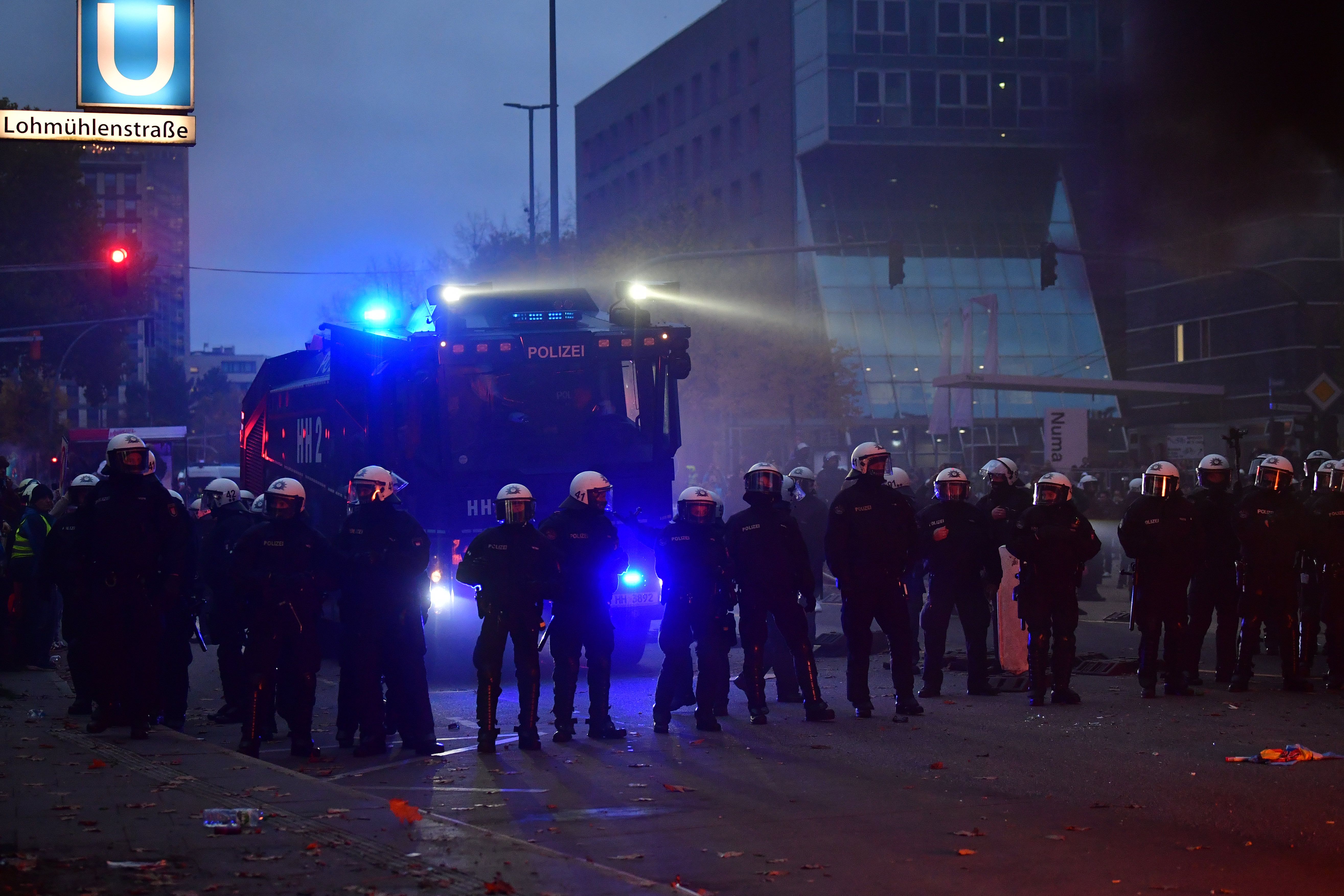 Polizisten in voller Ausrüstung und ein Wasserwerfer bei Protesten abends in Hamburg.
