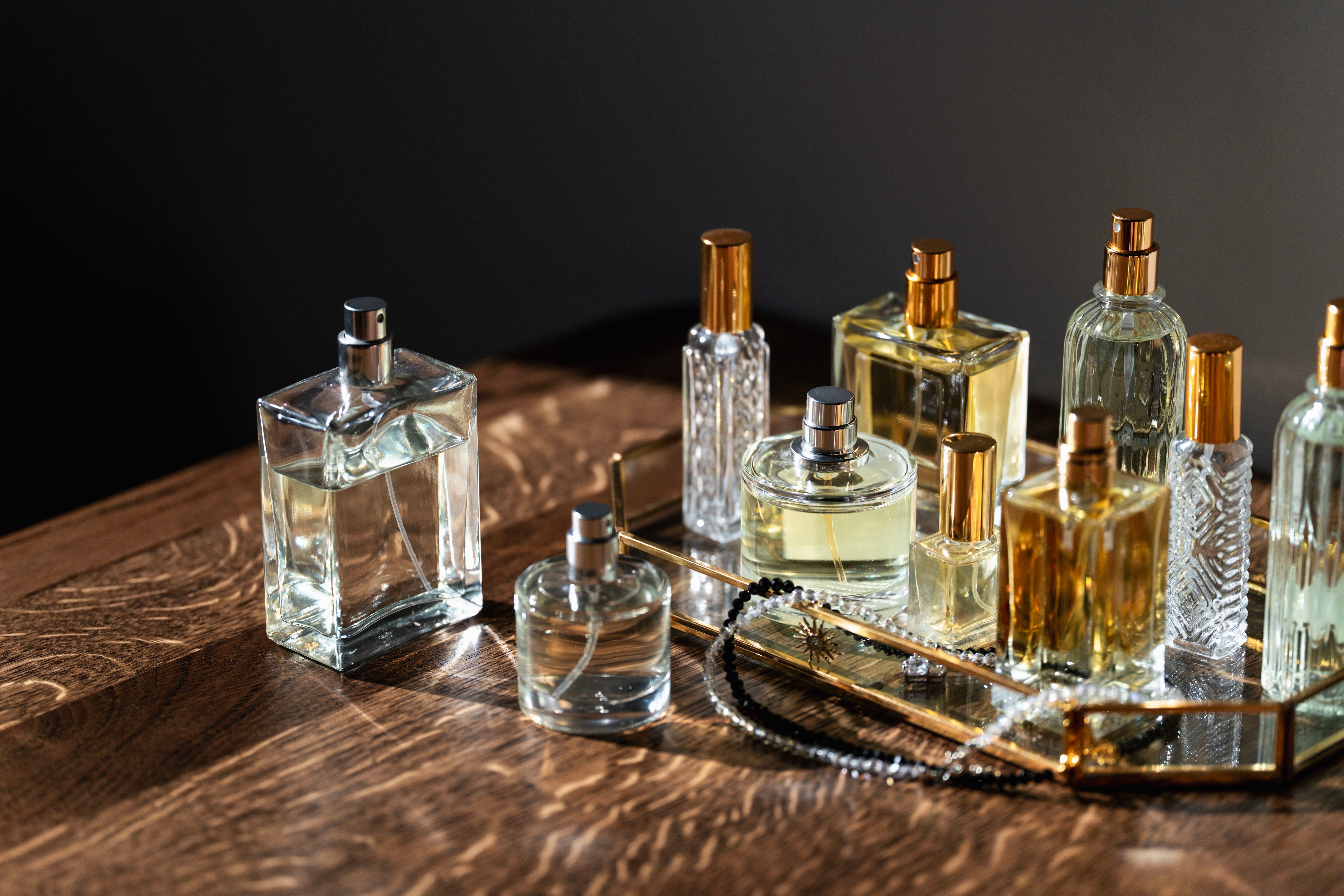 Verschiedene Glas-Parfümflakons stehen auf einem Holztisch und werden seitlich beleuchtet.