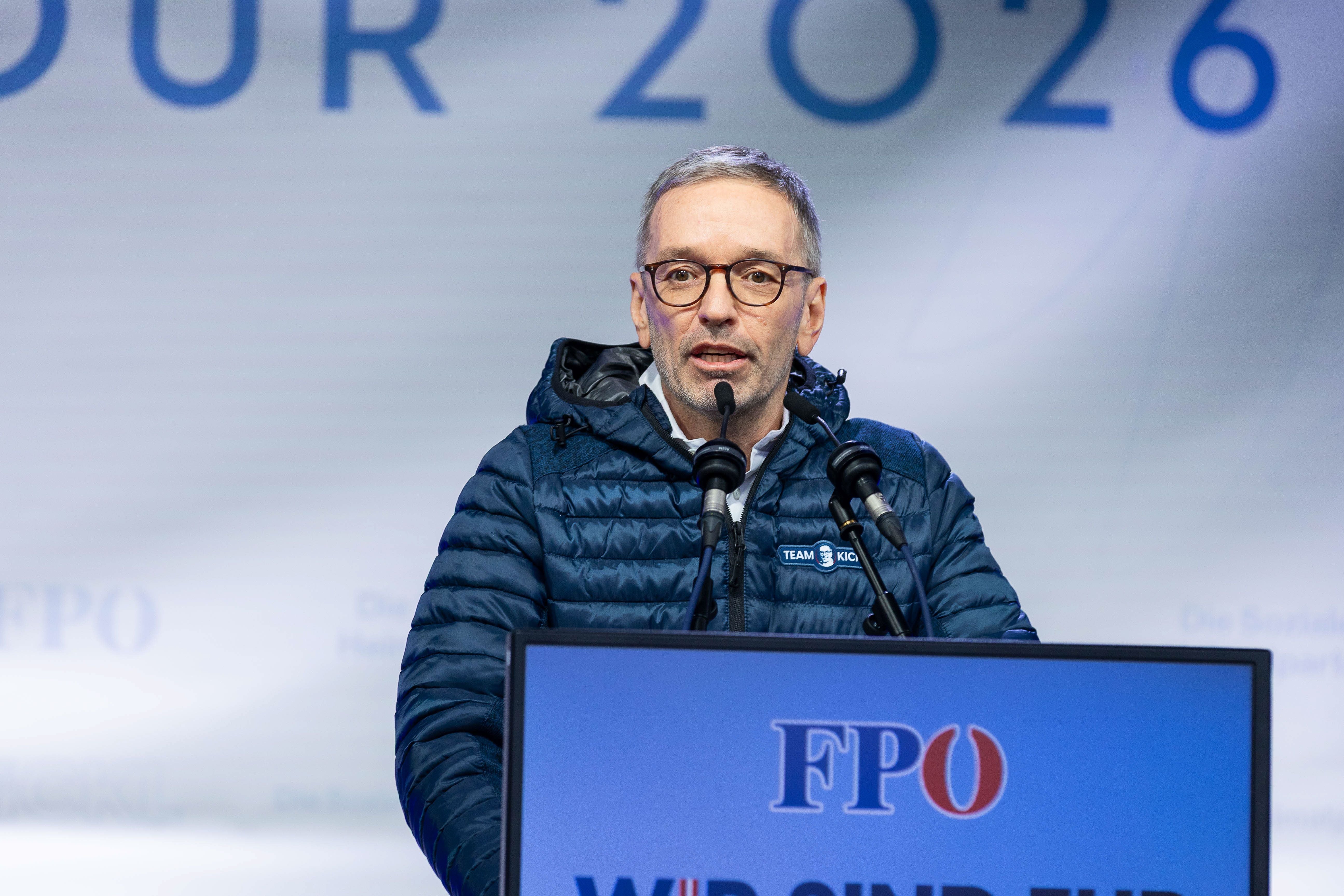 Ein Mann mit Brille spricht bei einer FPÖ-Veranstaltung am Rednerpult mit Mikrofonen.