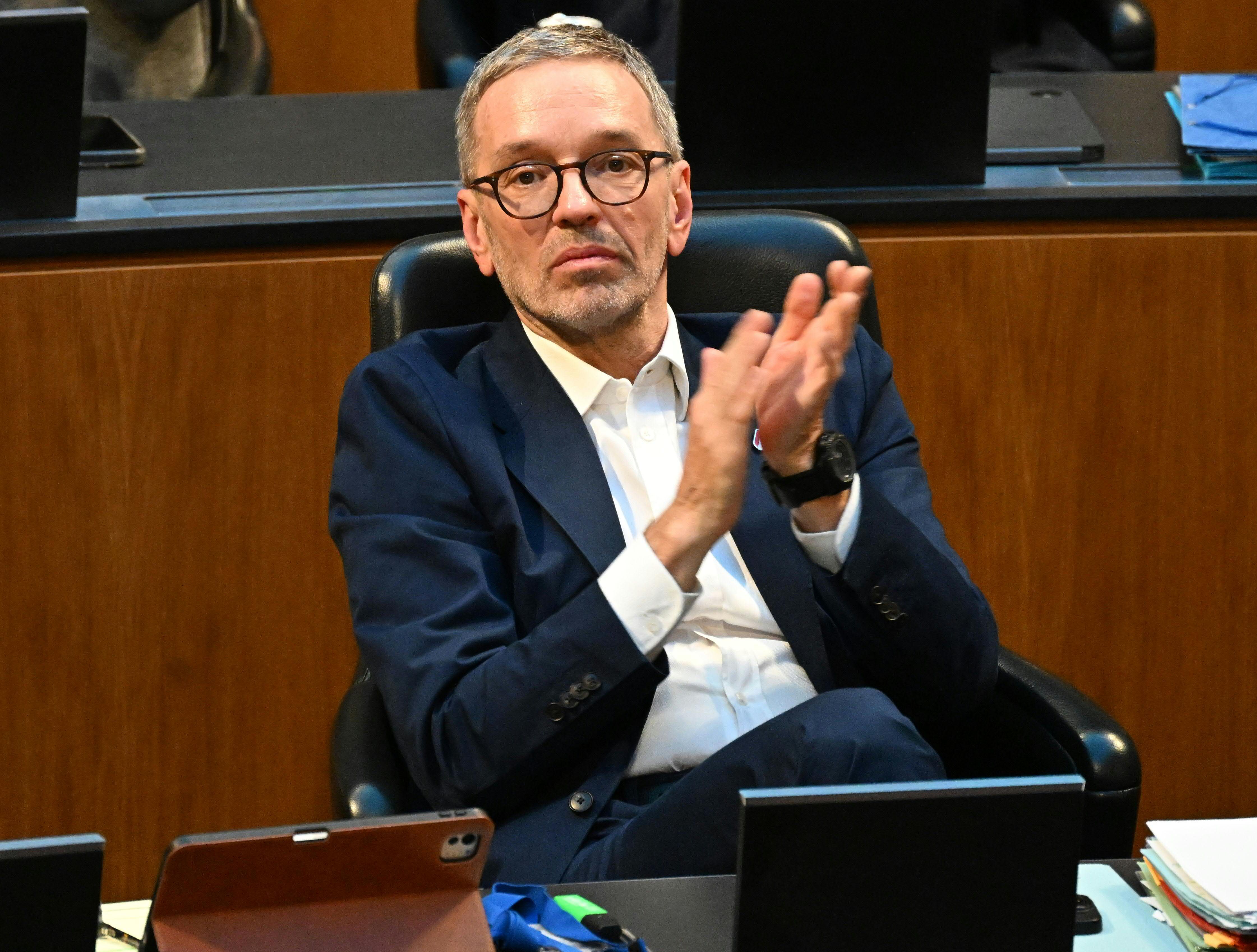 Ein Mann im Anzug sitzt im Parlament und klatscht in die Hände.